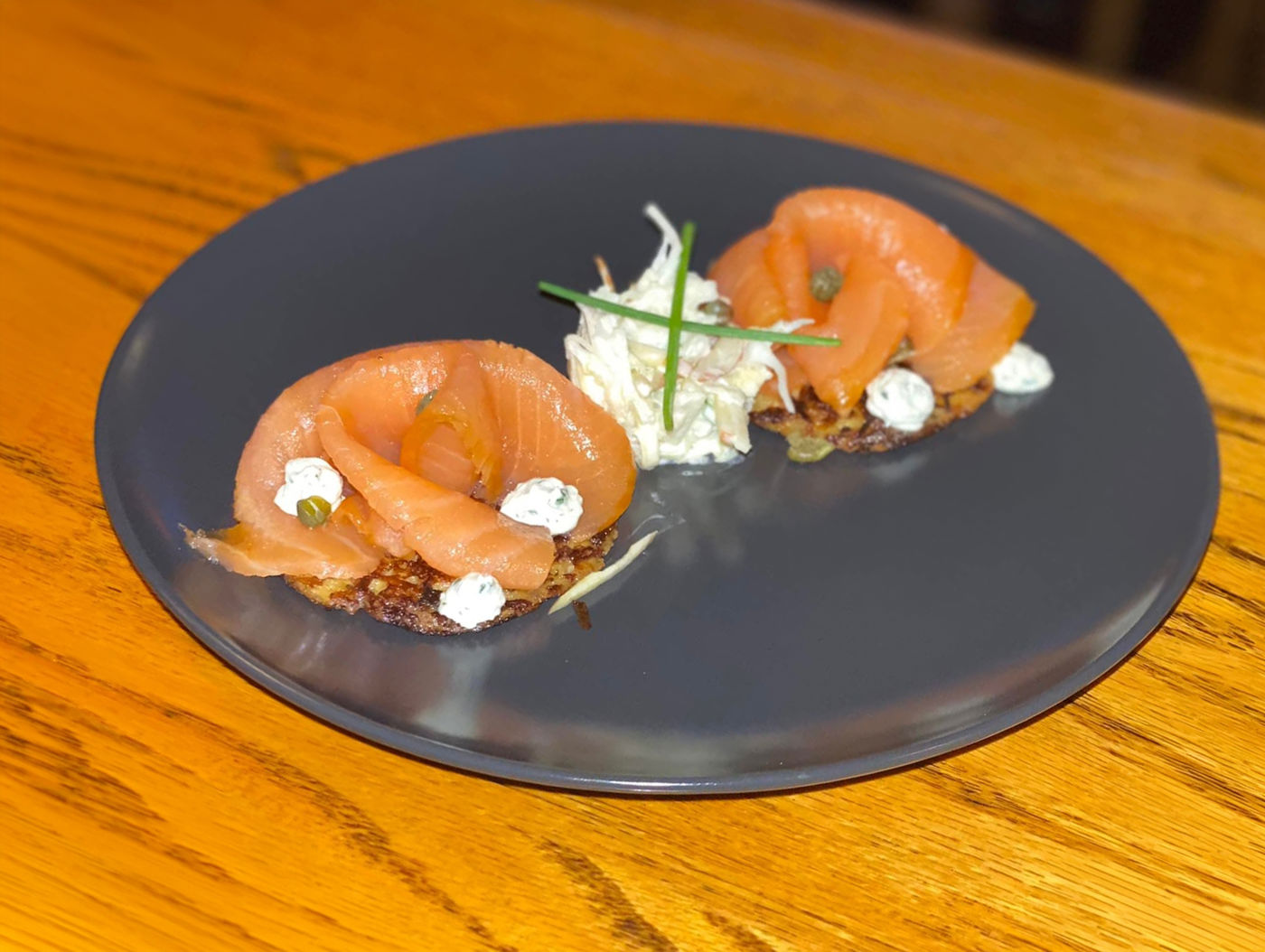 Gerecht met zalm en salade en roomkaas geserveerd op een zwart rond bord gegarneerd met kruiden Eetcafé De Drie Noten